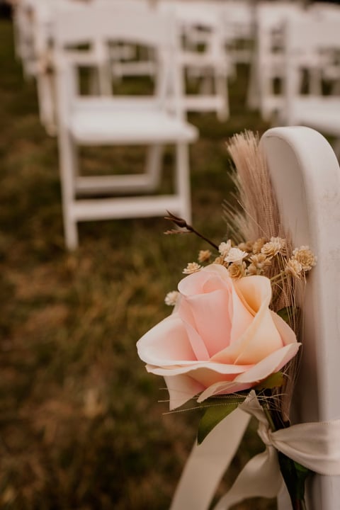 Pink rose with wheat and babys breath attached to a white wedding chair