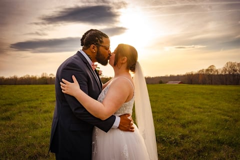 Bride and groom kissing in an open field at sunset