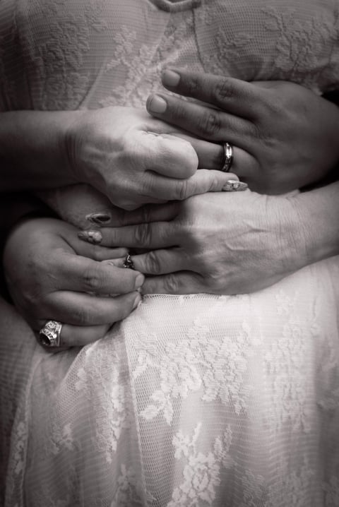 Black and white photo of a bride and groom displaying their wedding rings on lace dress