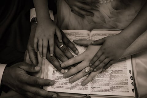 Multiple hands with wedding rings resting on an open book