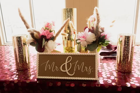 Wedding sweetheart table decorated with Mr and Mrs sign, pink flowers, pampas grass, gold candles, and glittery pink tablecloth