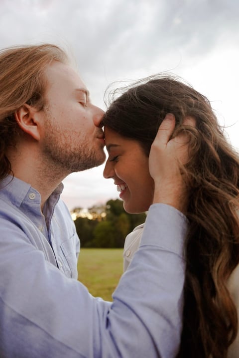 Man in light blue shirt kissing womans forehead outdoors