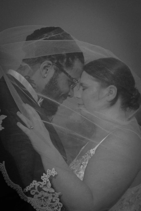 Black and white wedding photo of bride and groom kissing under veil