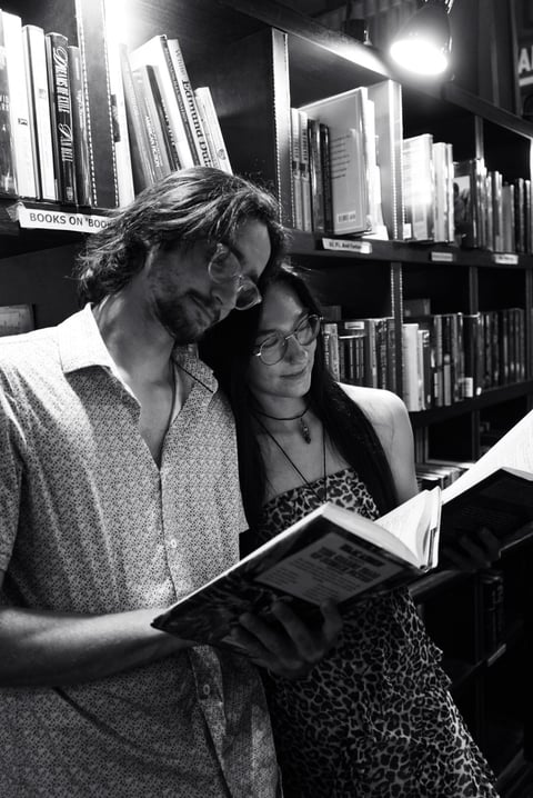Two people reading a book together in a library with illuminated bookshelves in the background