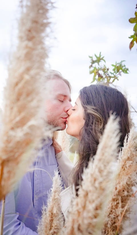 Couple kissing outdoors surrounded by dried ornamental grasses