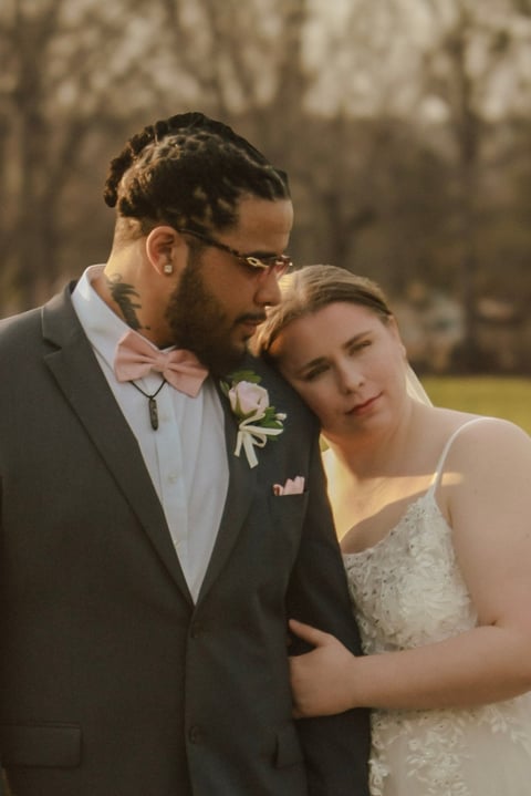 Groom in gray suit kisses bride in white beaded dress outdoors