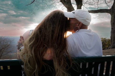 Couple sitting on bench at sunset overlooking a scenic landscape