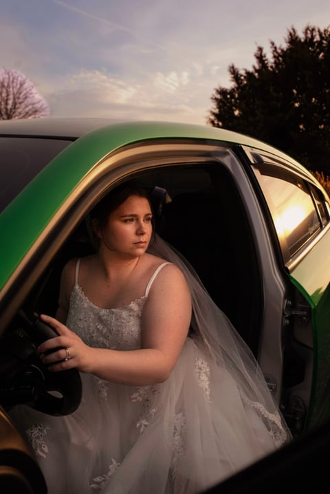 Woman in white dress sitting in drivers seat of green car at sunset