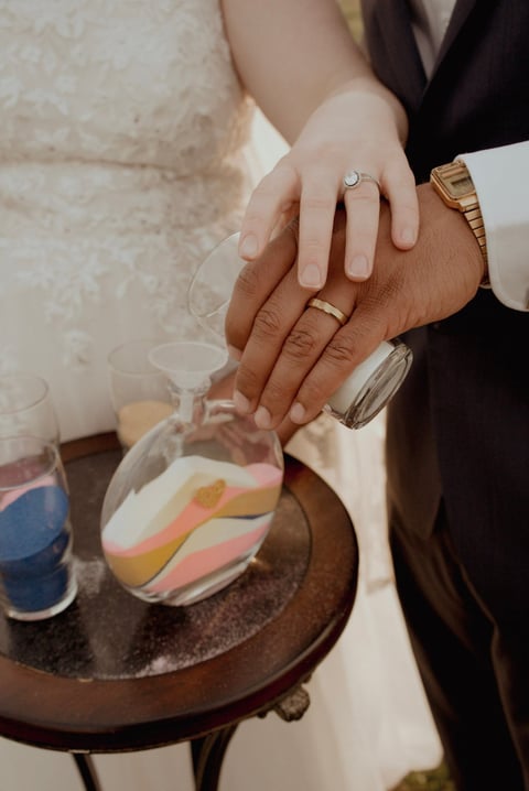 Newlyweds displaying wedding rings while holding hands over a colorful drink