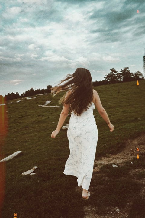 Woman in white dress walking through green hillside field
