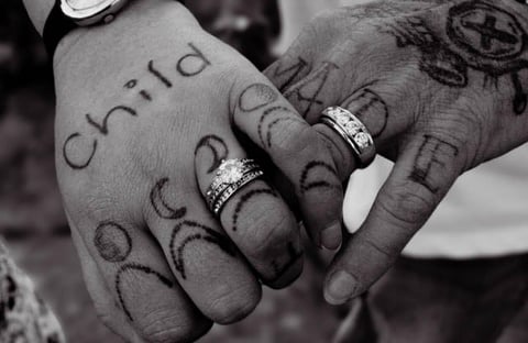 Close-up black and white image of two hands with wedding rings and tattoos