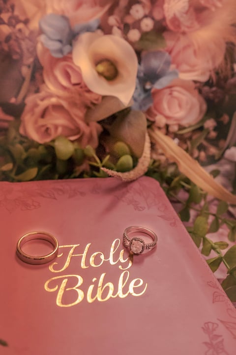 Wedding rings displayed on a pink Holy Bible with white and pink flowers